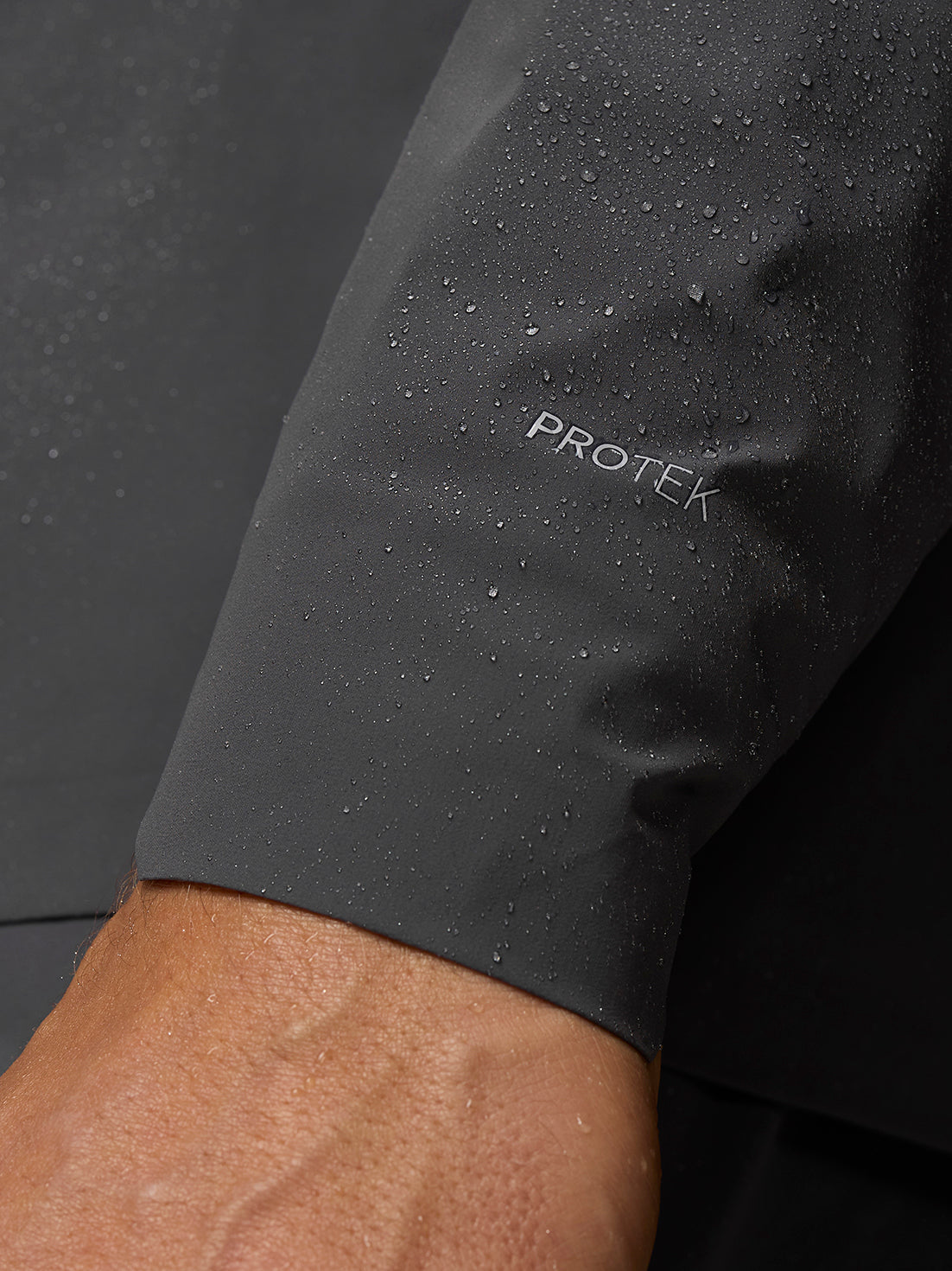 Close-up of Gunmetal/Black Reflective Zone LVS Jacket sleeve with PROTEK logo and water droplets.
