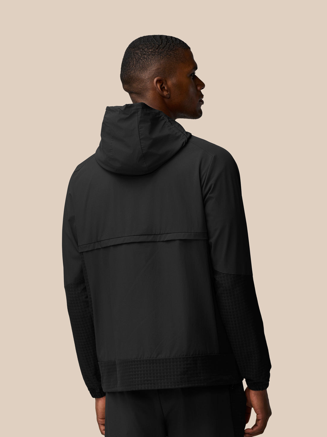 Back view of a man wearing black Flex Winterised Woven Jacket with hood showing rear hem and textured sleeves