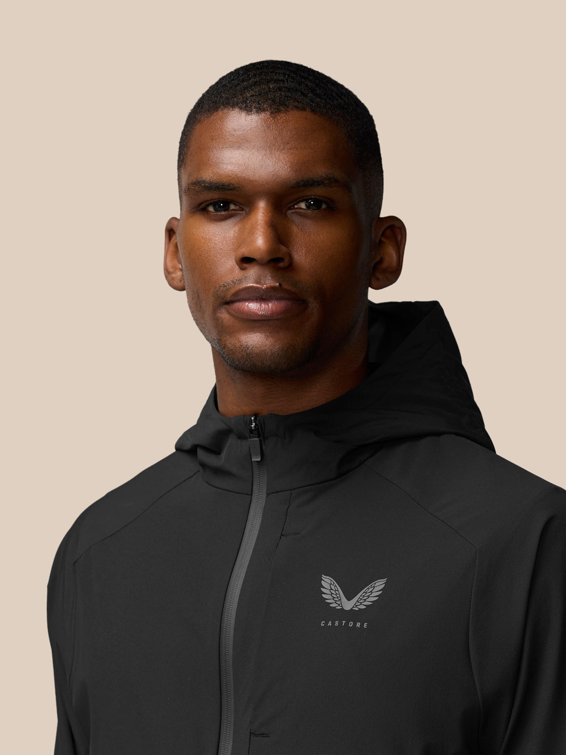 Close-up of a man wearing a black Flex Winterised Woven Jacket with hood, Castore logo visible on left chest.