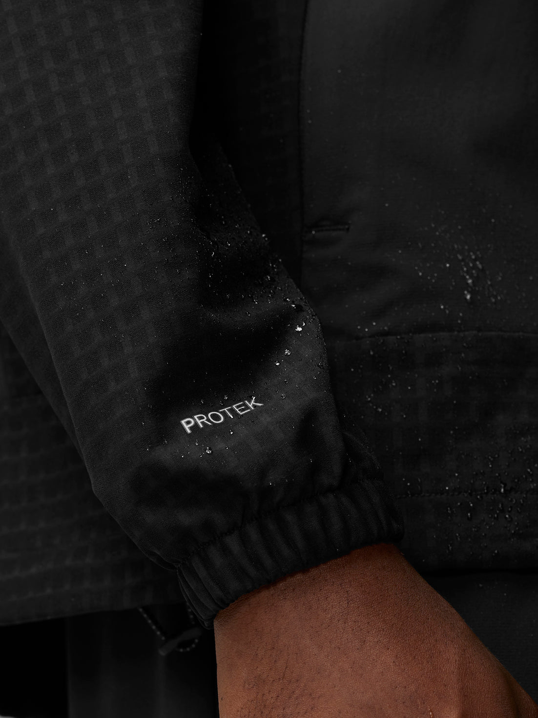 Sleeve cuff of black Flex Winterised Woven Jacket with ProTek badge and water droplets