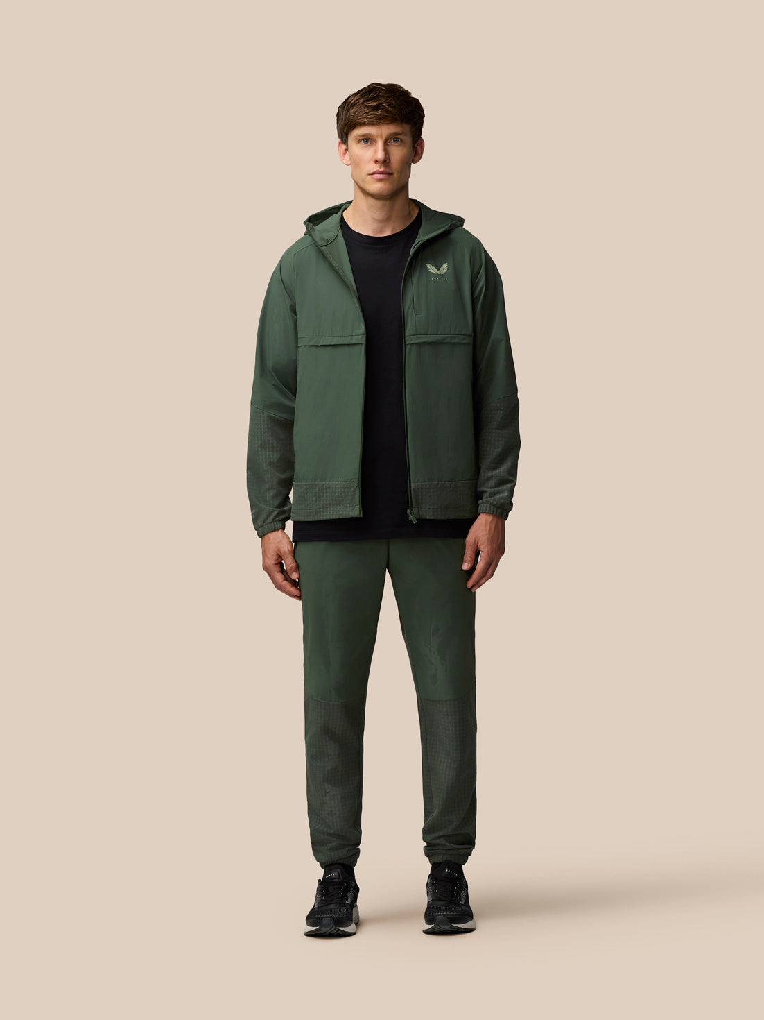 Back view of a man wearing the dark green Flex Winterised Woven Jacket with hood and textured hem panels