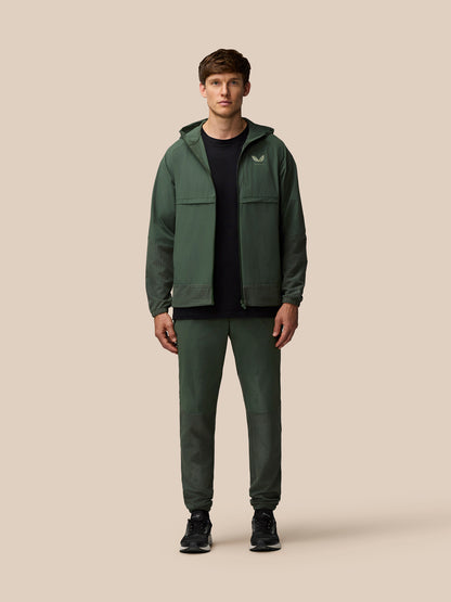 Back view of a man wearing the dark green Flex Winterised Woven Jacket with hood and textured hem panels