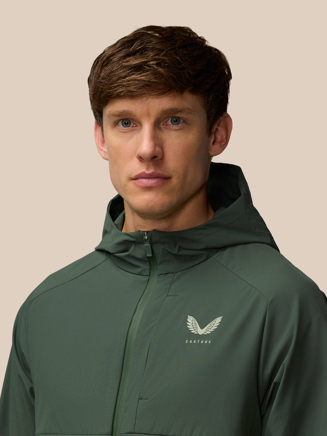 Male model wearing dark green Flex Winterised Woven Jacket with hood and Castore logo on the chest.