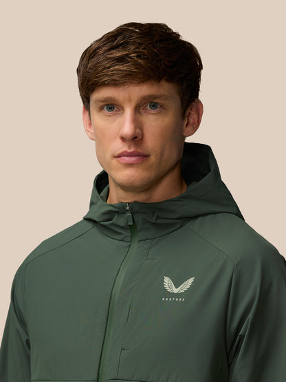 Male model wearing dark green Flex Winterised Woven Jacket with hood and Castore logo on the chest.