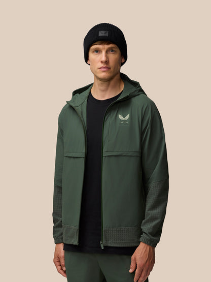 Male model in dark green Flex Winterised Woven Jacket with hood down, Castore logo on left chest, wearing a black beanie.