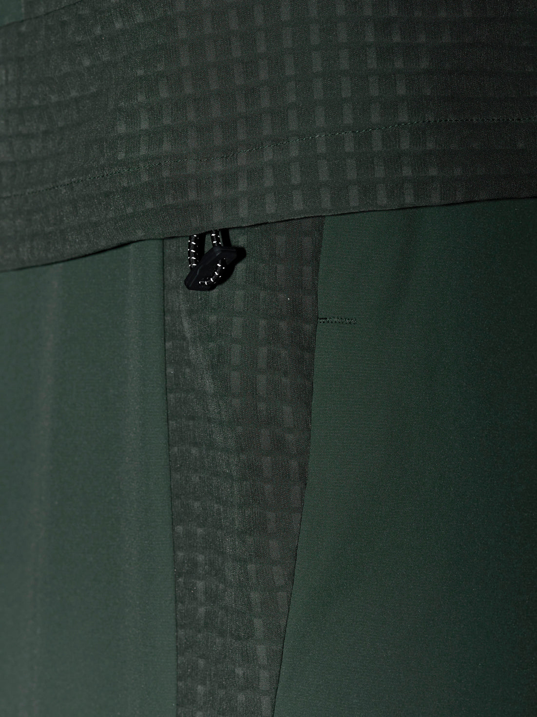 Zipper pull on dark green Flex Winterised Woven Jacket with grid textured fabric.