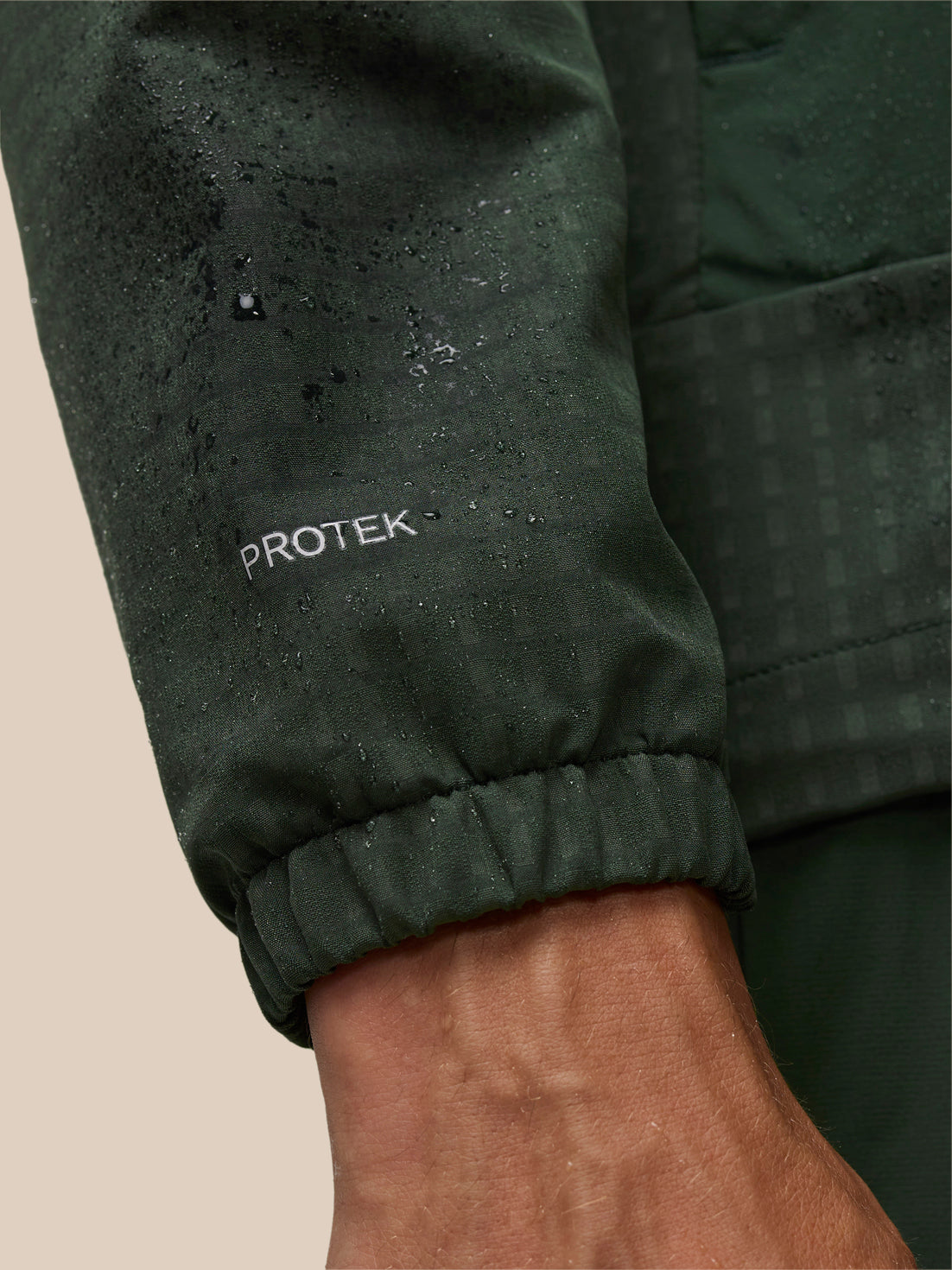 ProTek logo on the sleeve of a dark green jacket with water droplets on the fabric and an elastic cuff.