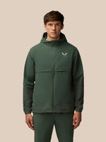 Front view of a man wearing a dark green Flex Winterised Woven Jacket with hood and Castore logo on the chest