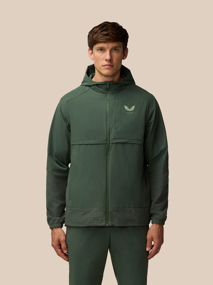 Front view of a man wearing a dark green Flex Winterised Woven Jacket with hood and Castore logo on the chest
