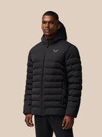 Man in black lightweight padded jacket with hood and front zipper against a beige background