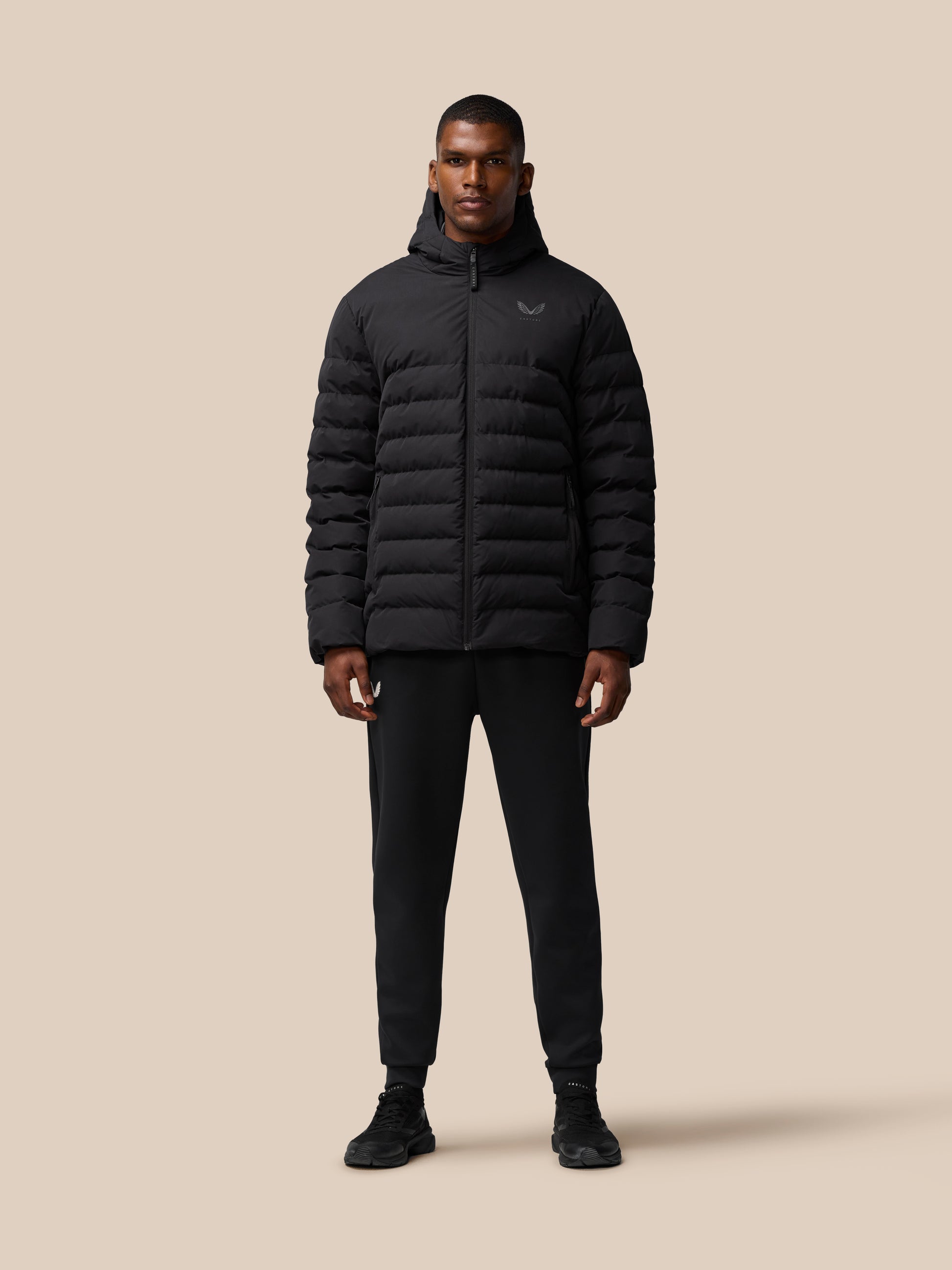 Three-quarter front view of a man in a black puffer jacket with hood and zip details