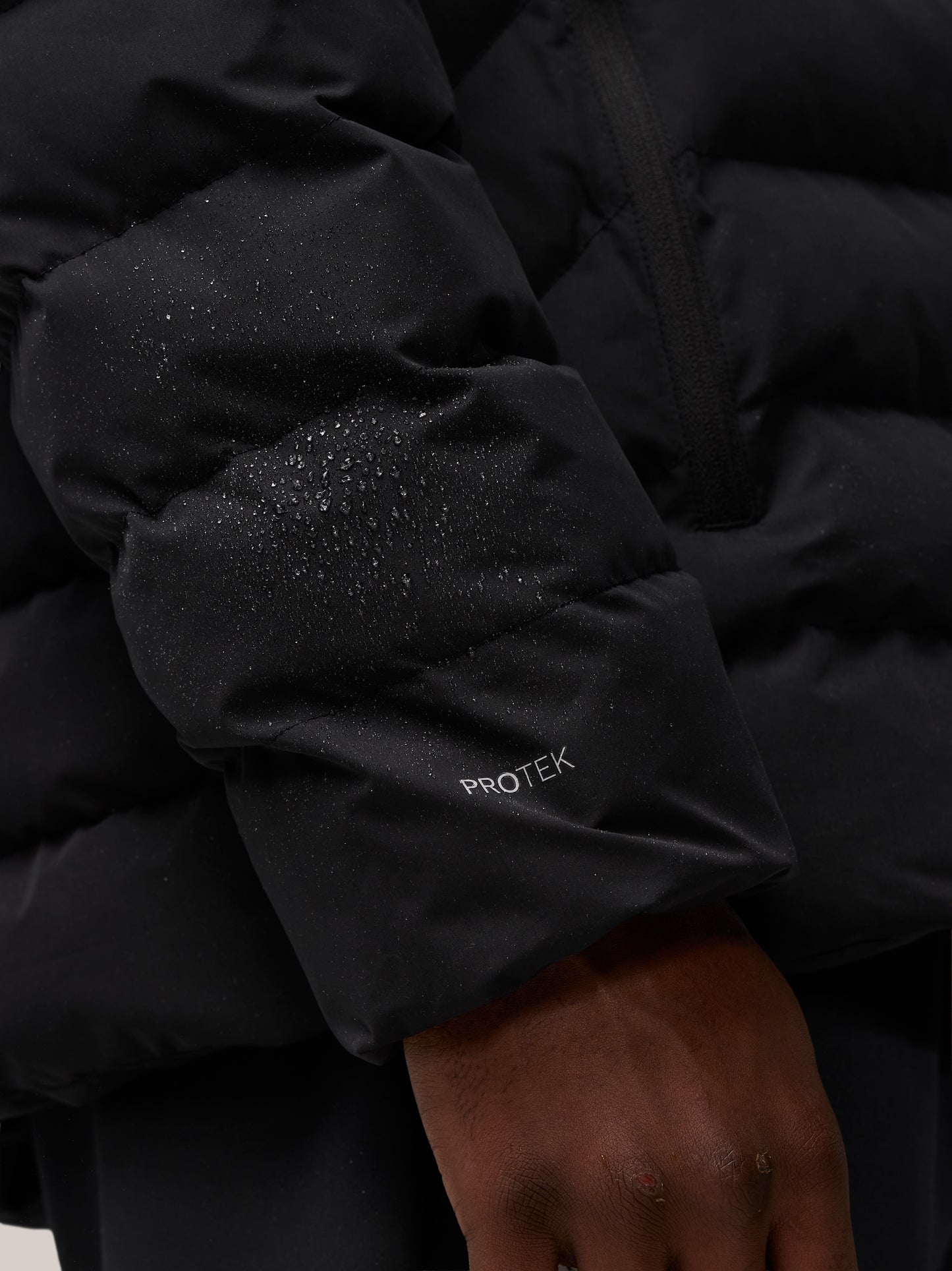 Close-up of a black lightweight puffer jacket sleeve with water droplets and ProTek branding.