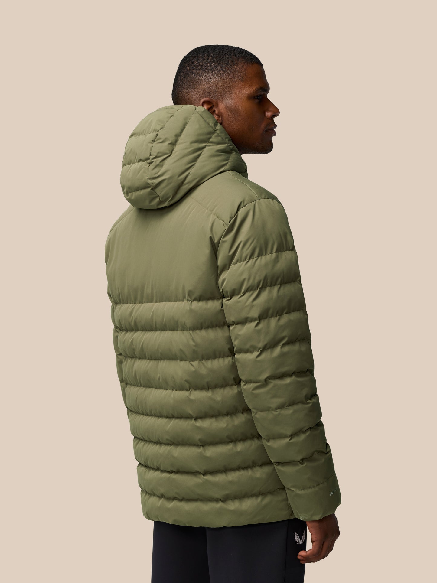 Man wearing ivy green lightweight puffer jacket with hood, shown in a side profile highlighting quilted panels.