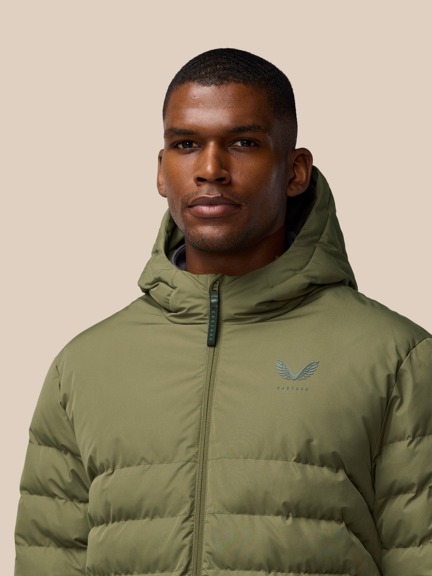 Close-up of a man wearing an ivy green lightweight puffer jacket with a hood and chest logo.