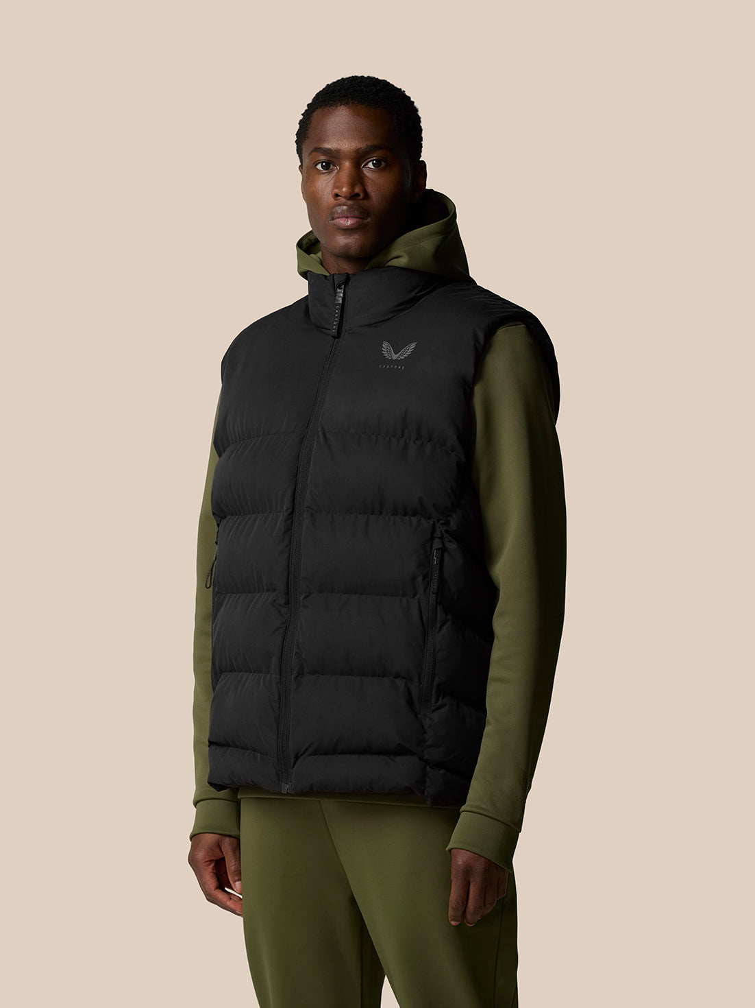 Close-up of male model in black puffer gilet with hood and front zip, chest logo visible