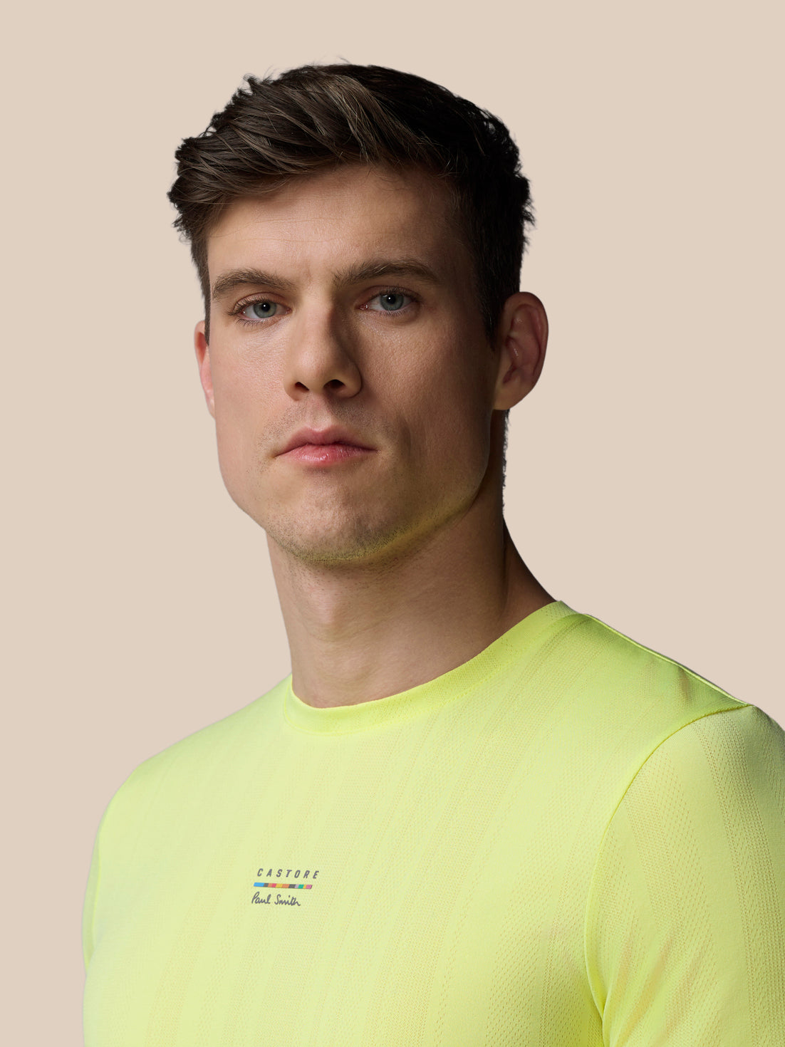 Male model wearing neon lime knit short sleeve T shirt with Castore x Paul Smith branding on chest.
