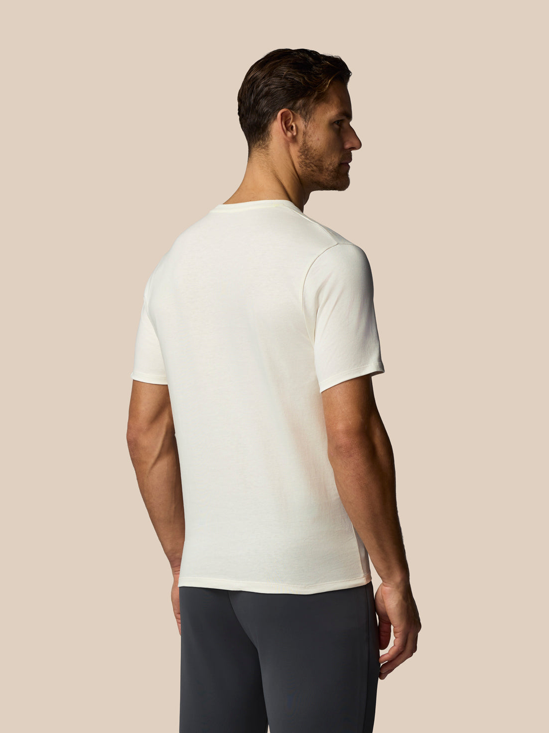 Man wearing a white t-shirt and dark pants against a beige background