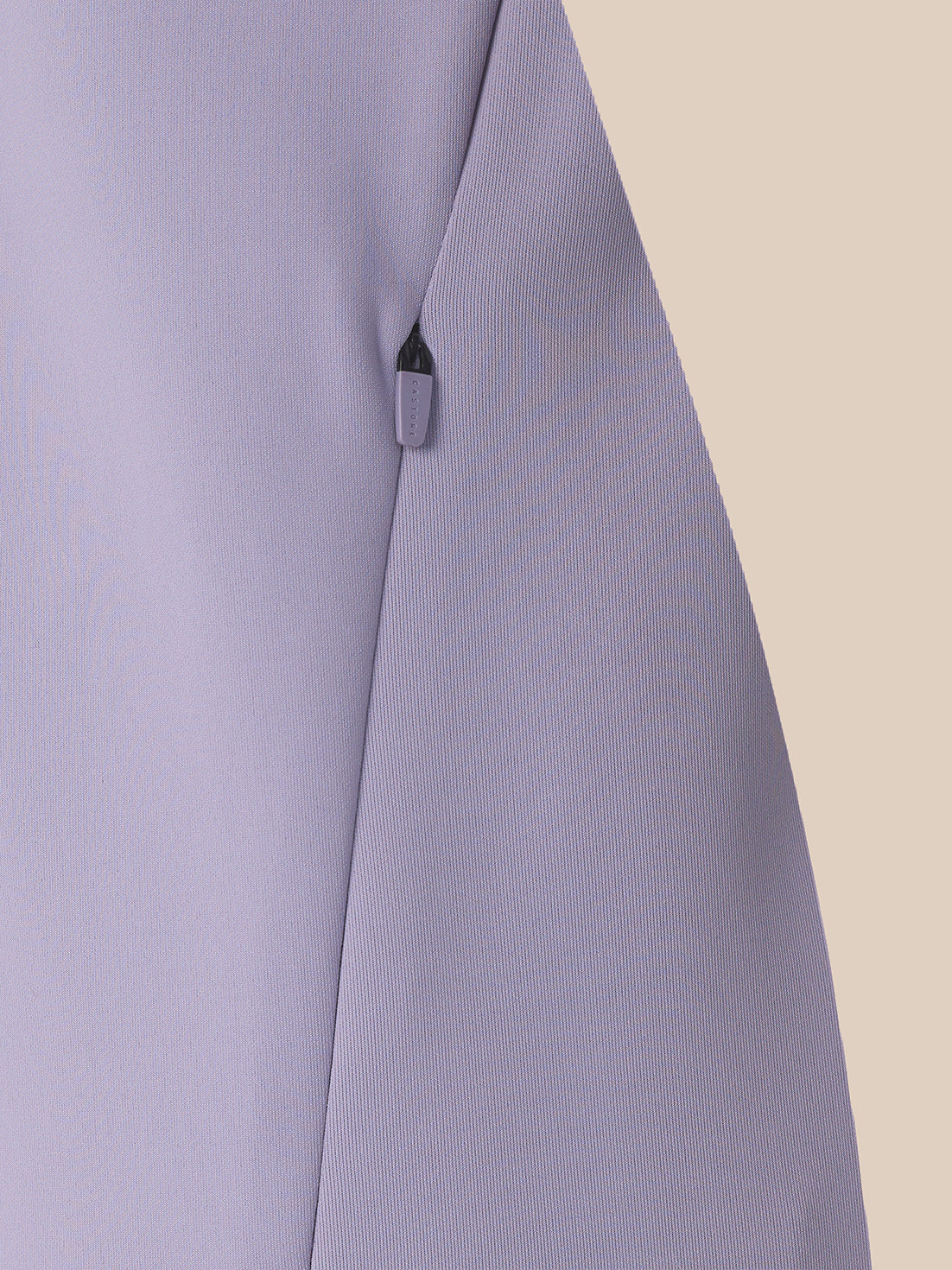 Close-up of a light lavender-gray fabric garment with a visible dark zipper pull on a plain beige background.