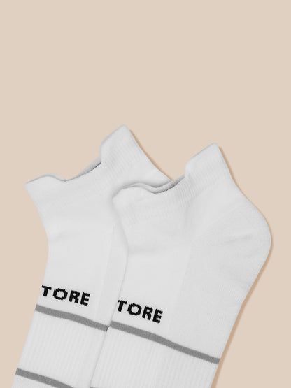 Close-up of two white ankle socks with gray cuff stripes on a beige background