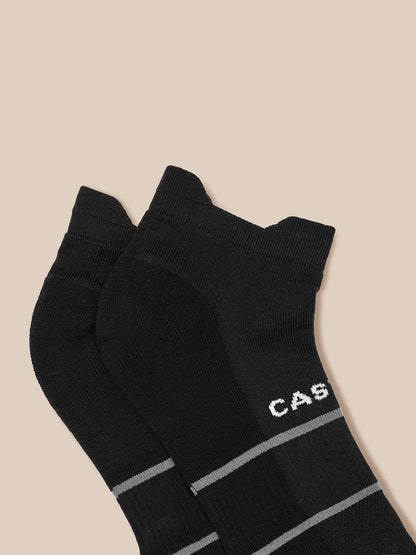 Two black ankle socks with gray stripes and Castore branding on a beige backdrop