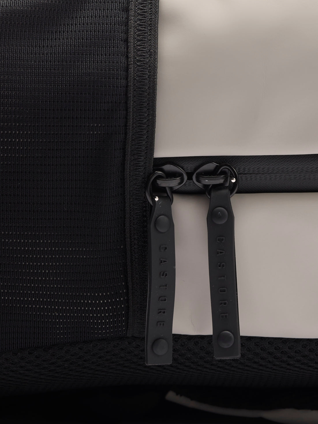 Close up of two CASTORE zipper pulls on black strap against beige fabric