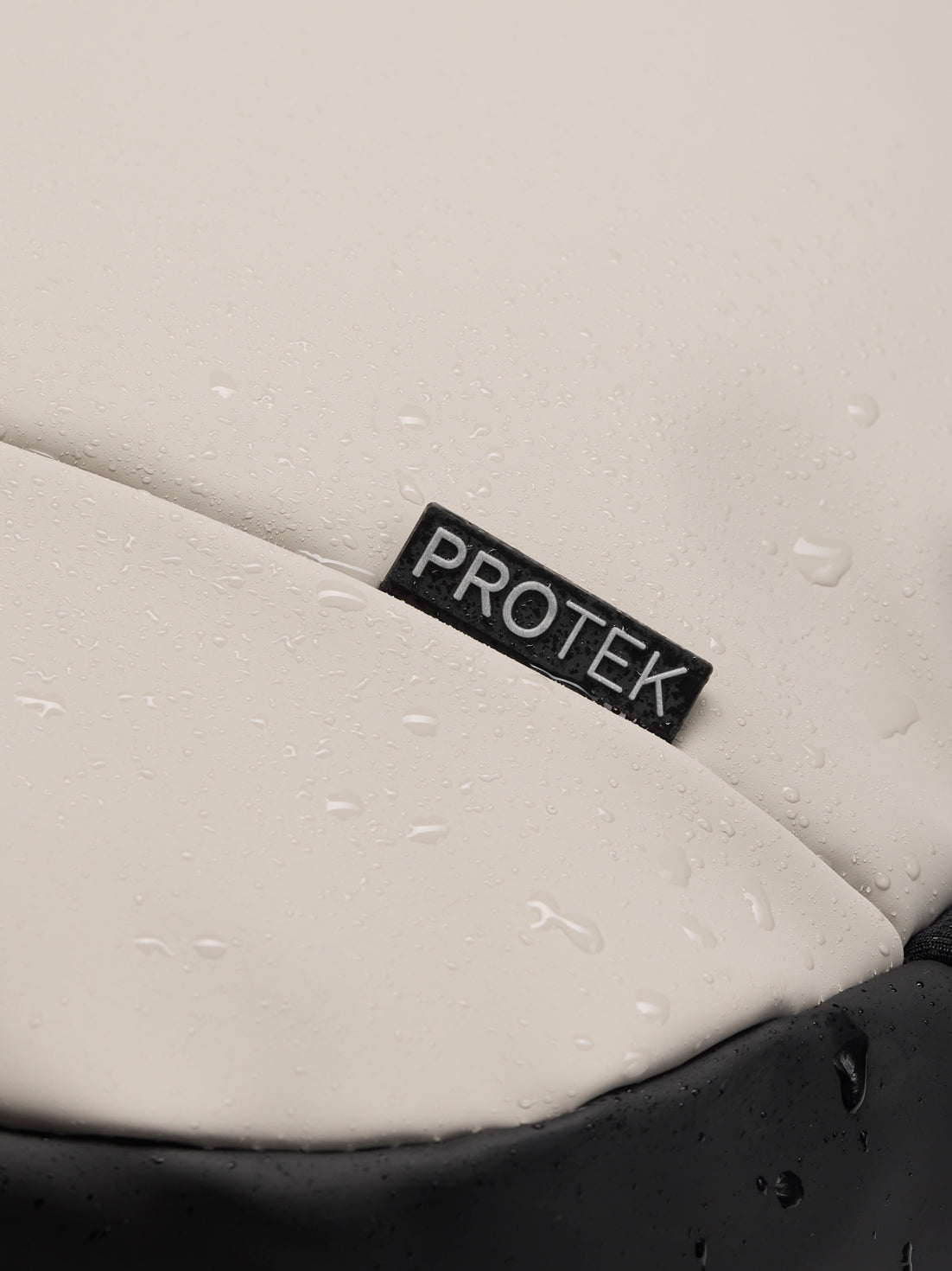 Close up of black ProTek label on light grey backpack fabric with water droplets