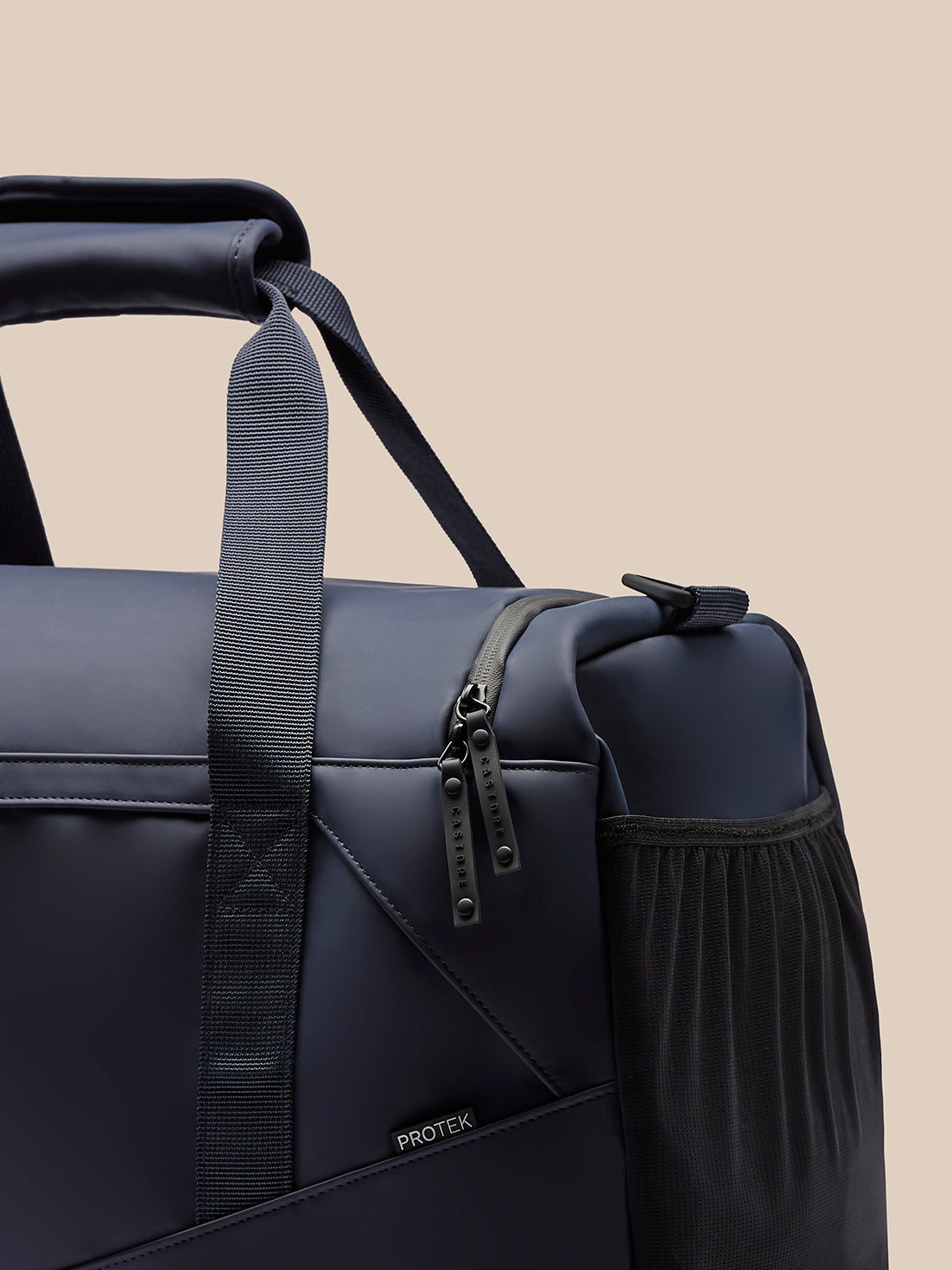 Close-up of navy holdall showing padded handles and gear-style zipper pulls on the side pocket