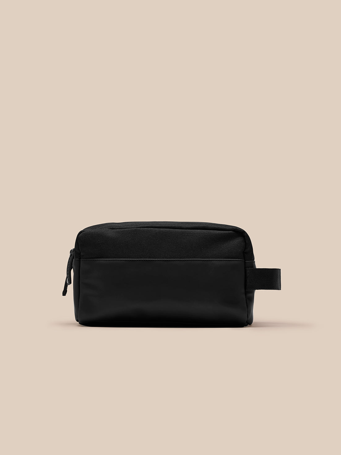 Compact black Core Wash Bag with zip closure and side strap on beige background