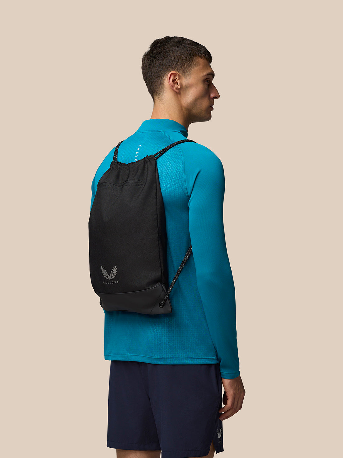 Model wearing black Castore Active Training Gymsack on back with blue athletic top