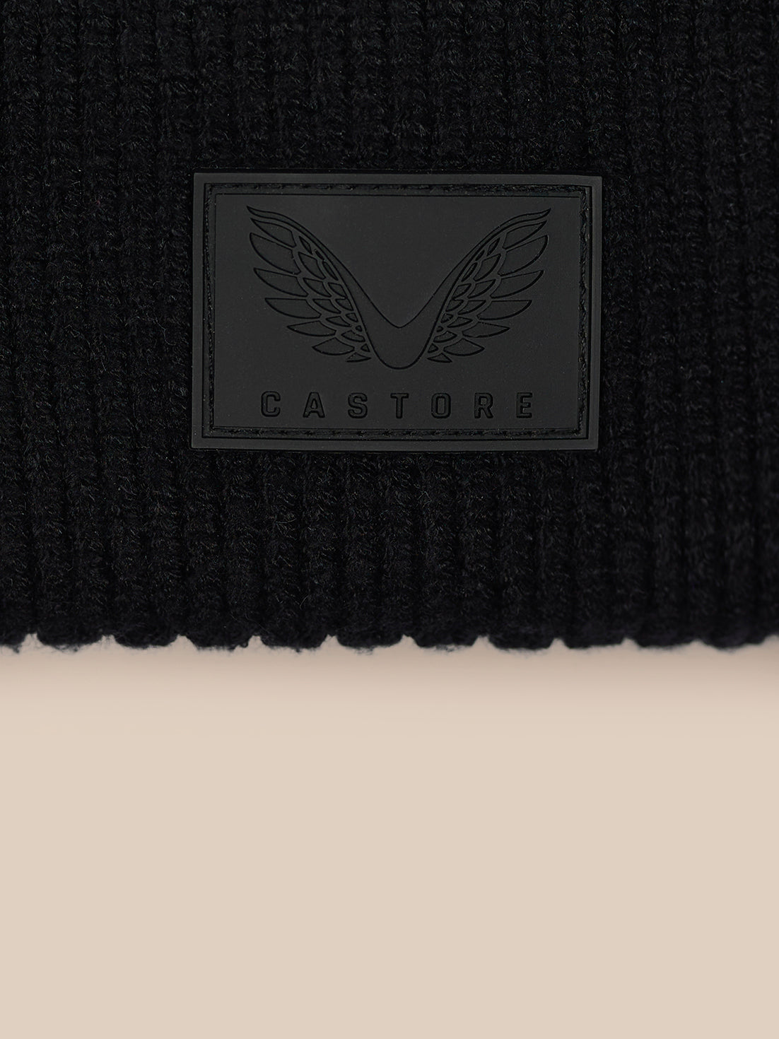 Close up of black ribbed Castore beanie with rectangular logo patch on front