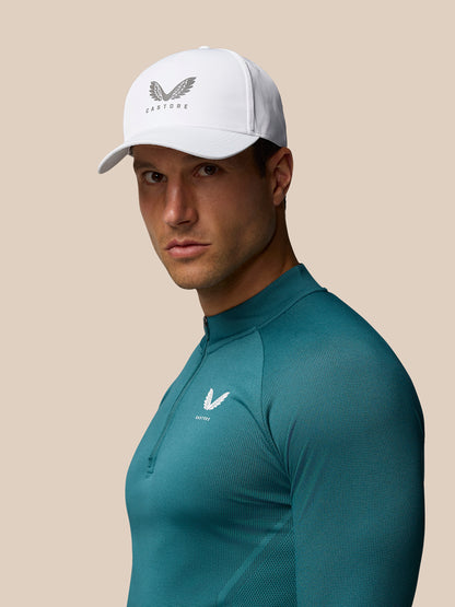 Model wearing white Castore Core Cap with winged logo and teal athletic top