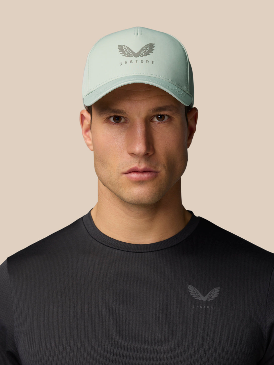 Male model wearing sage Active Cap with Castore logo, close-up portrait.