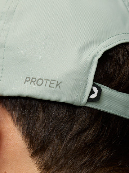 Close-up of the back of a sage cap showing PROTEK branding on the strap and a small winged badge