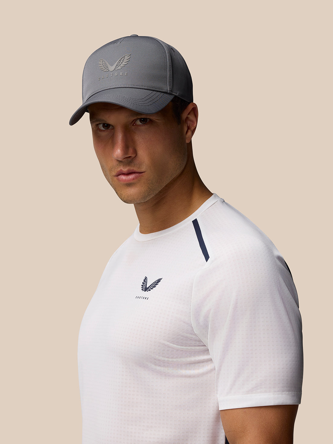 Male model wearing a charcoal Cap with halo eyelets and adjustable back strap; Castore logo on front.