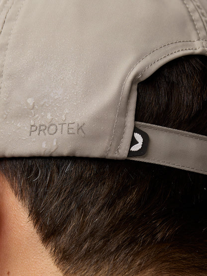 Close-up of rock grey cap fabric with PROTEK embossing and a small wing emblem at the back strap.