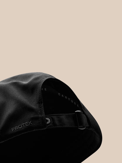 Close up side view of black cap showing adjustable strap buckle and PROTEK branding