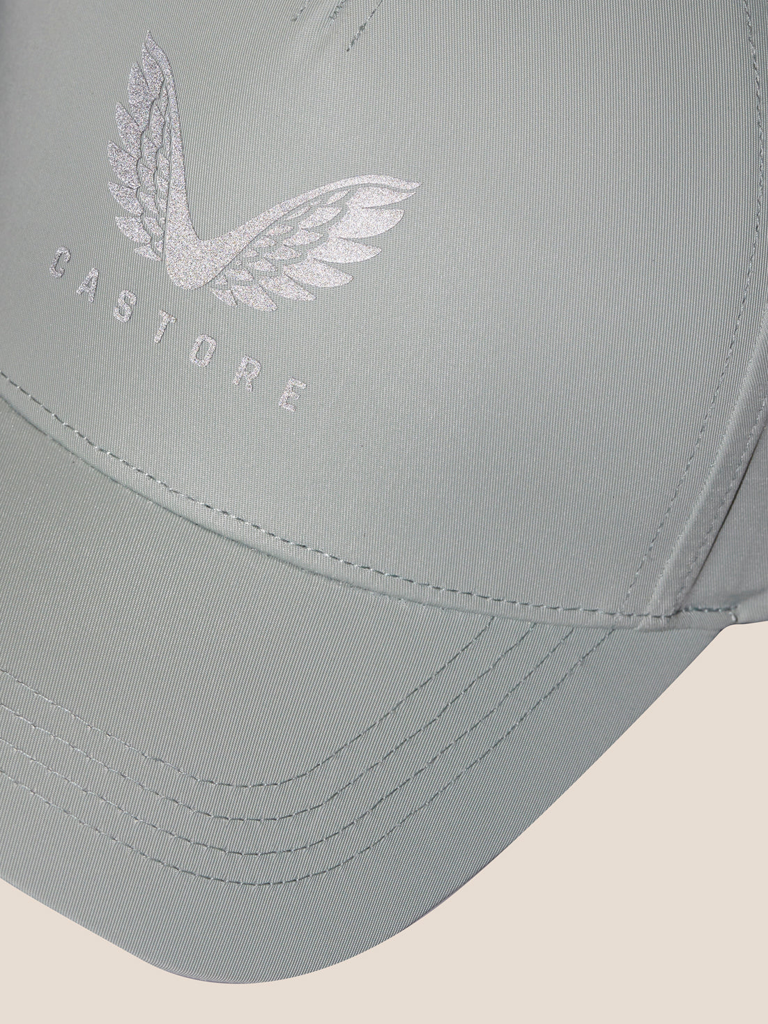 Close-up of the sage cap front displaying the embroidered Castore logo with wings.