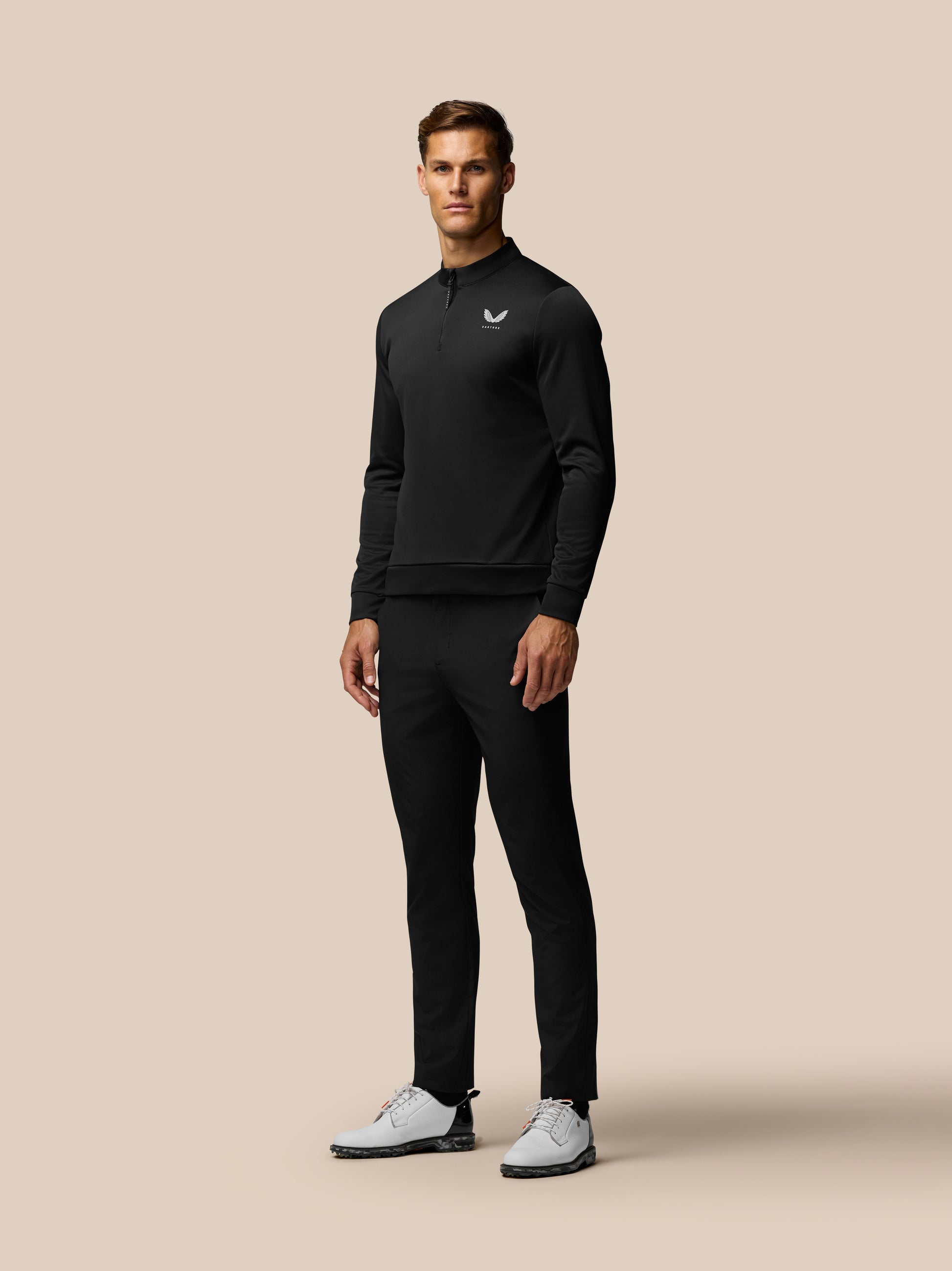 Male model wearing a black zip neck golf pullover with Castore logo on the chest.