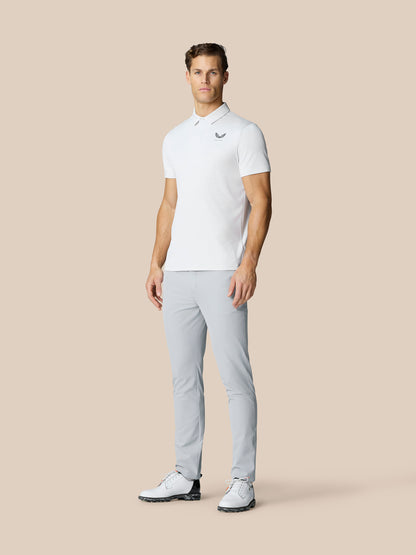 Full body shot of a man in light grey Castore Golf Club Trousers and a white polo, standing in golf shoes.