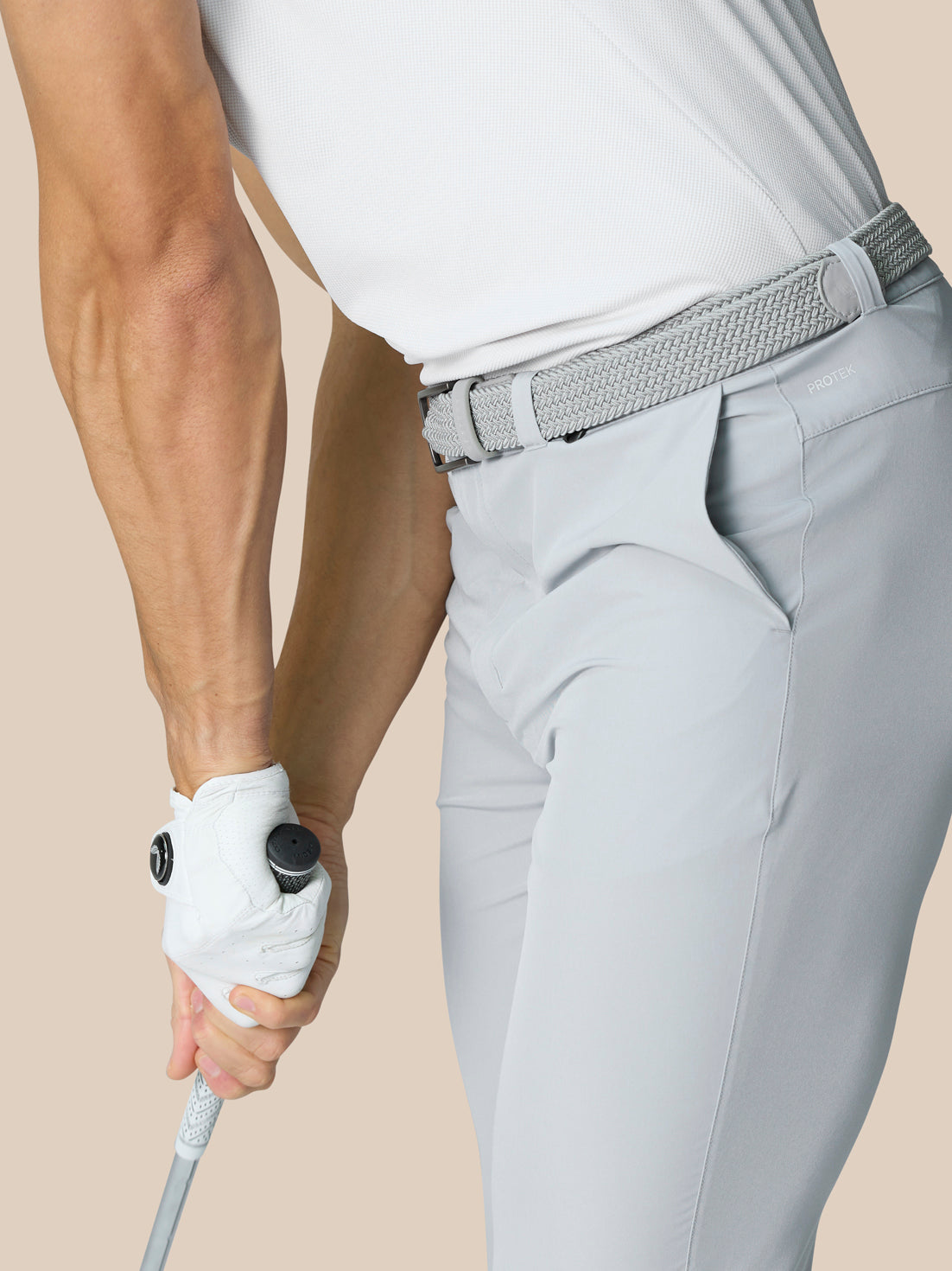 Side view of a man wearing light grey golf trousers with a woven belt and ProTek branding at the waistband.