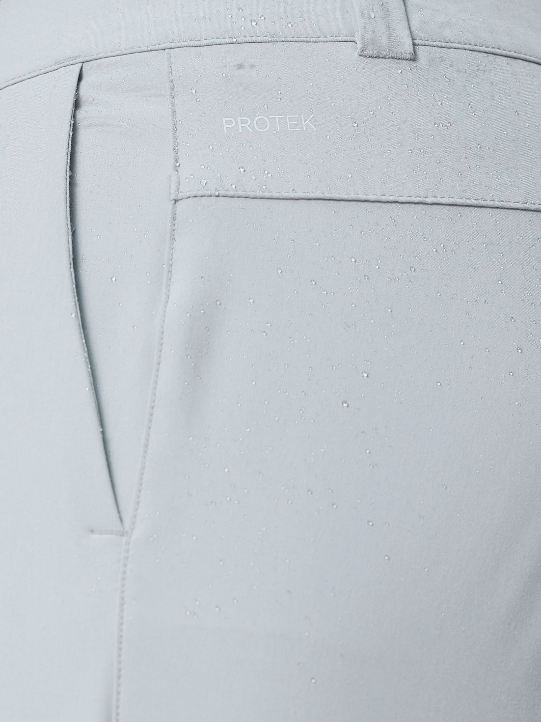 Close up of ProTek water resistant fabric on light grey golf trousers with water droplets.