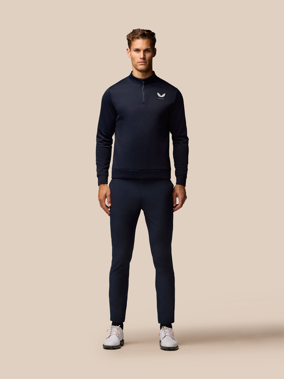 Male model in navy Castore golf outfit with a quarter zip top and matching trousers showing logos on chest and pocket
