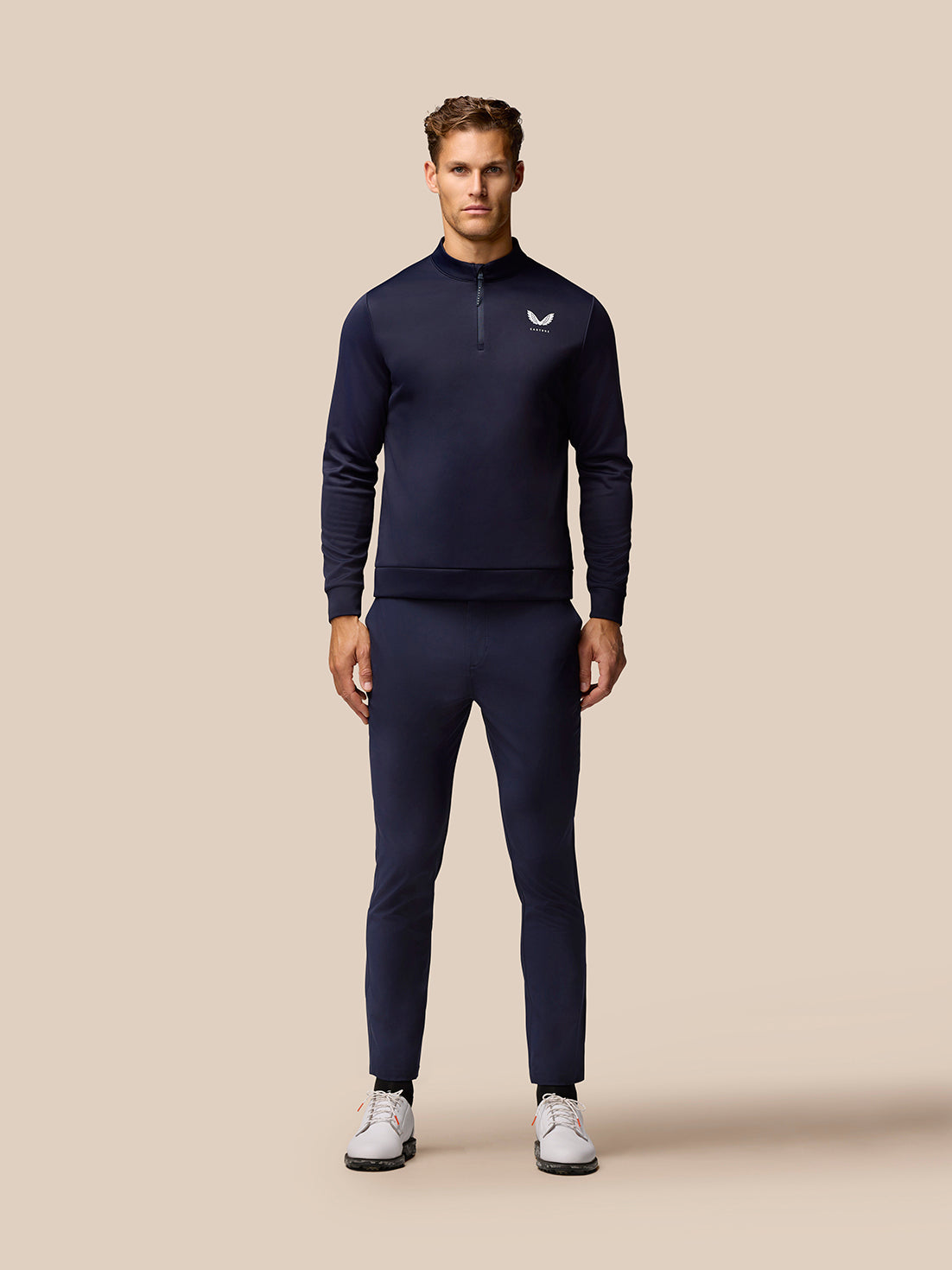 Male model in midnight navy golf outfit featuring a zip neck pullover and matching Golf Lightweight Club Trousers with white sneakers.