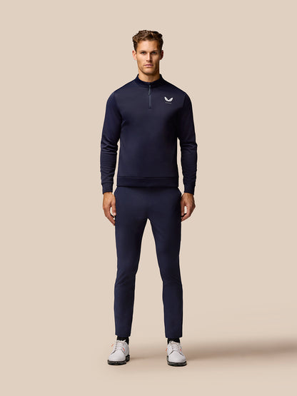 Male model in midnight navy golf outfit featuring a zip neck pullover and matching Golf Lightweight Club Trousers with white sneakers.
