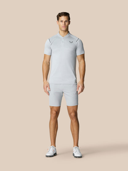 Man wearing light grey golf polo and matching shorts with Castore logo on chest against a beige backdrop