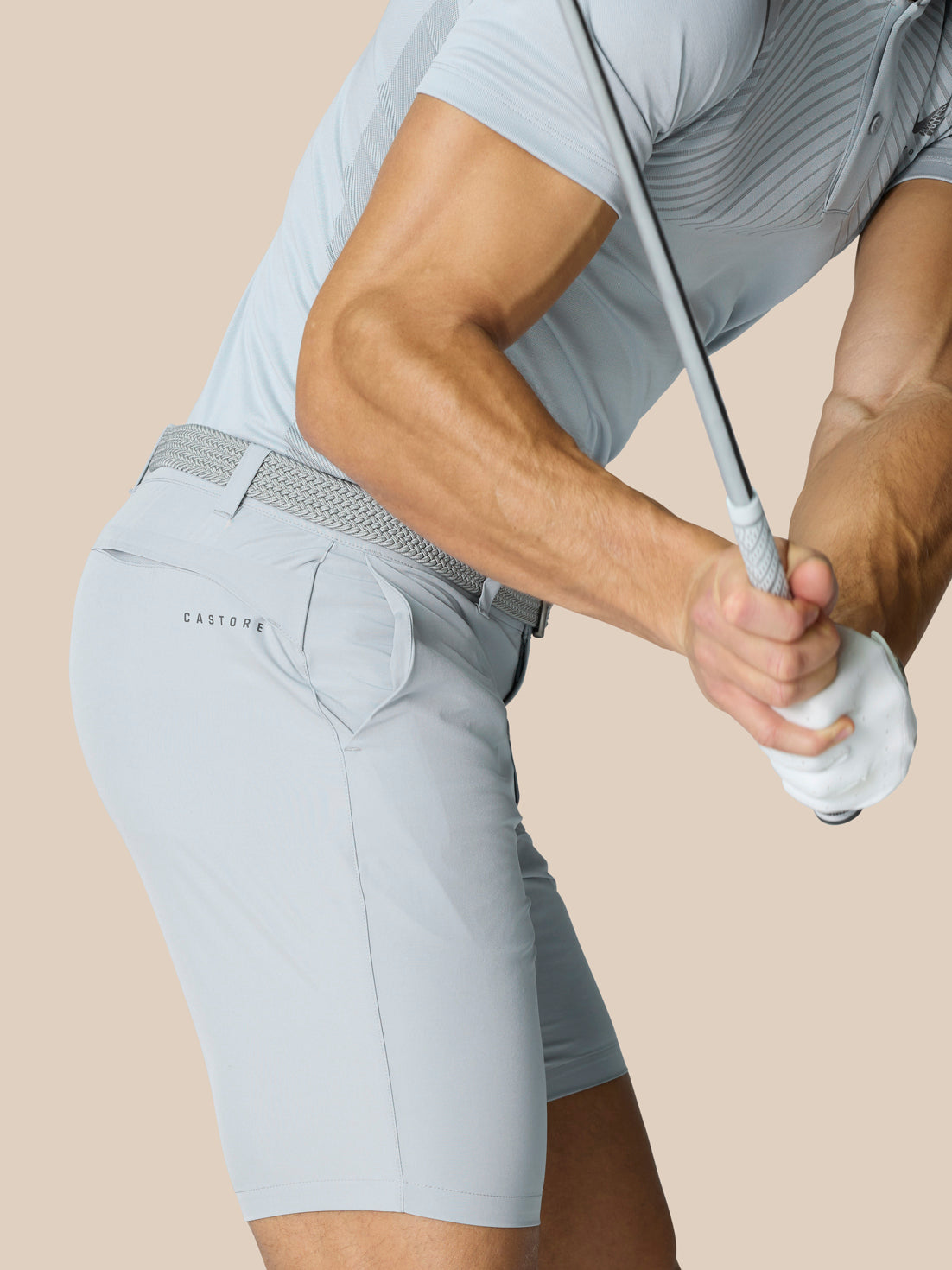 Side view of a man wearing light grey golf shorts with braided belt and Castore branding at the rear.