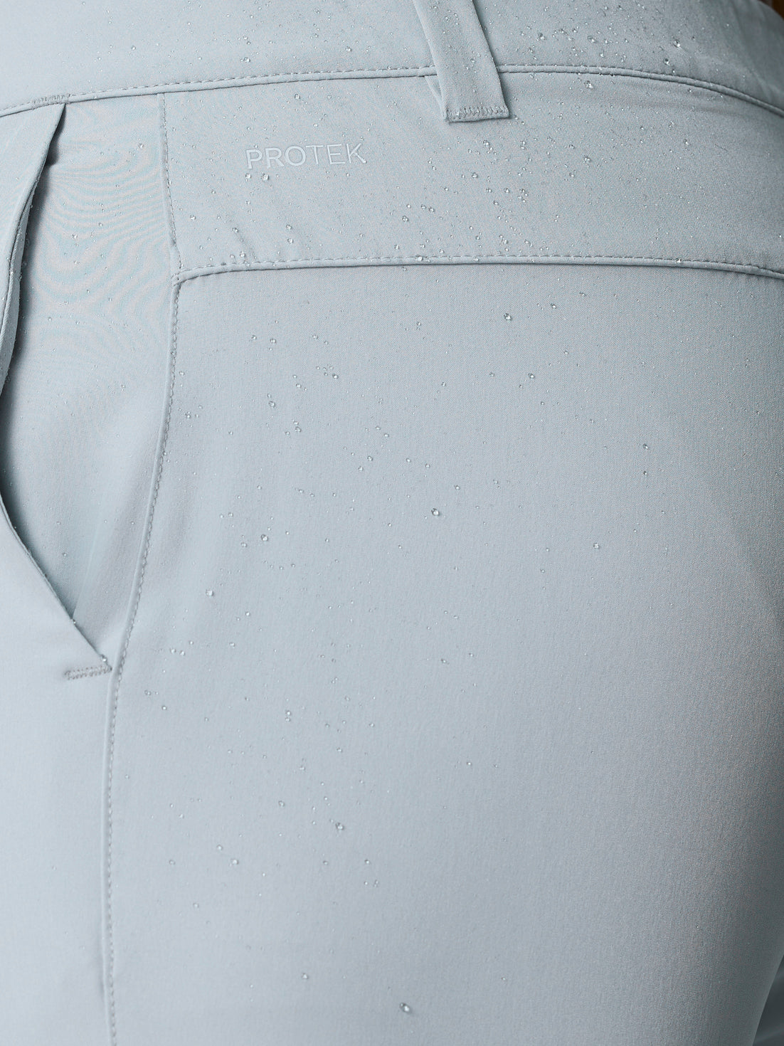 Close-up of light grey golf shorts back panel with PROTEK logo and water droplets on fabric.