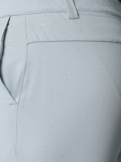 Close-up of light grey golf shorts back panel with PROTEK logo and water droplets on fabric.