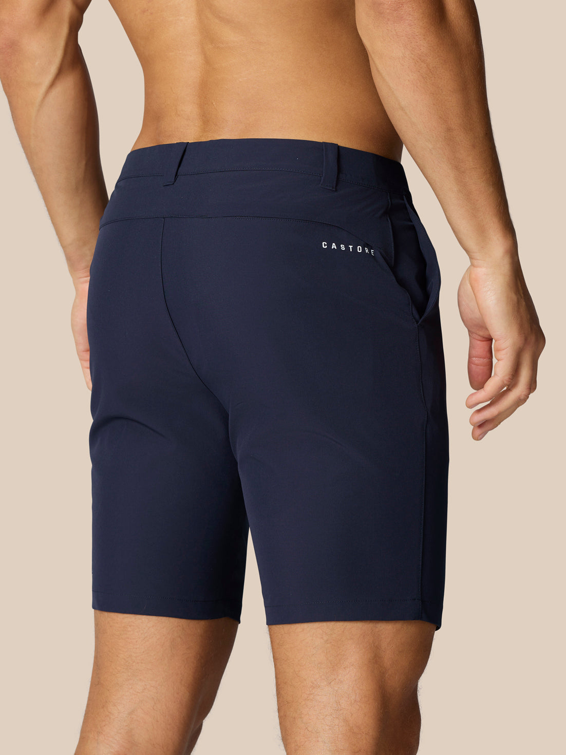 Back view of navy Castore golf shorts with belt loops, Castore branding on the right thigh and rear, and ProTek branding at the left rear waistband