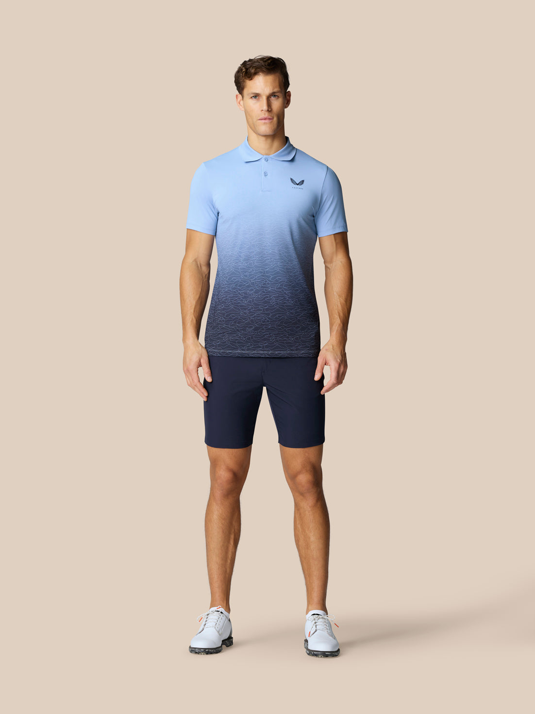 Male model wearing a light blue to navy gradient golf polo and navy shorts